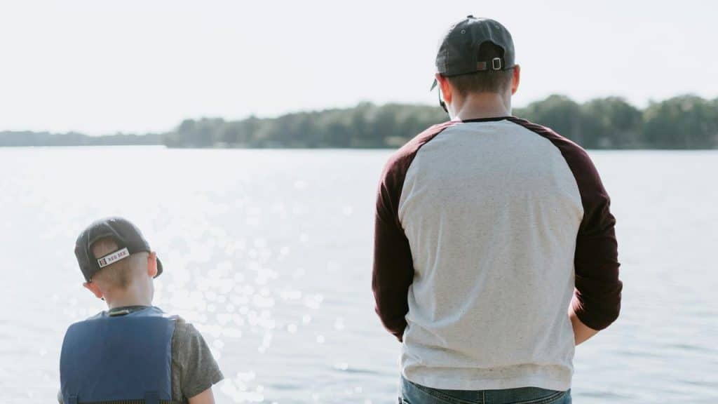 A man and a boy standing by a lake.
