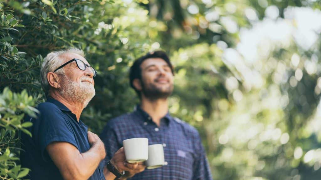 An older man and a younger man holding coffee mugs outdoors.