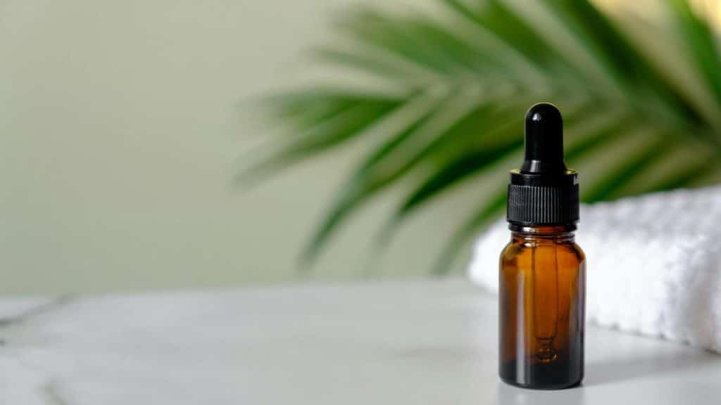 An amber glass dropper bottle on a white countertop with a blurred palm leaf in the background.