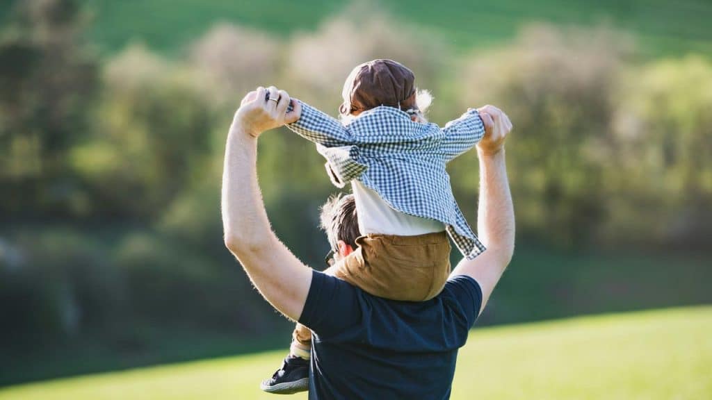 A child riding on an adult’s shoulders in a sunny field.