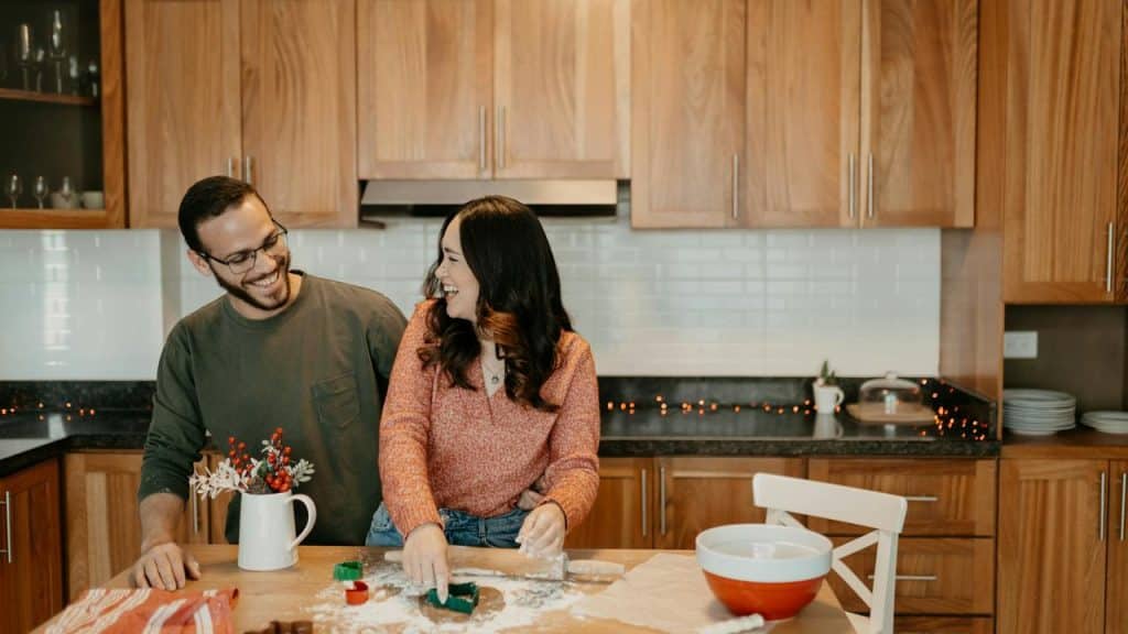 A couple laughing while cutting cookie dough in a kitchen.