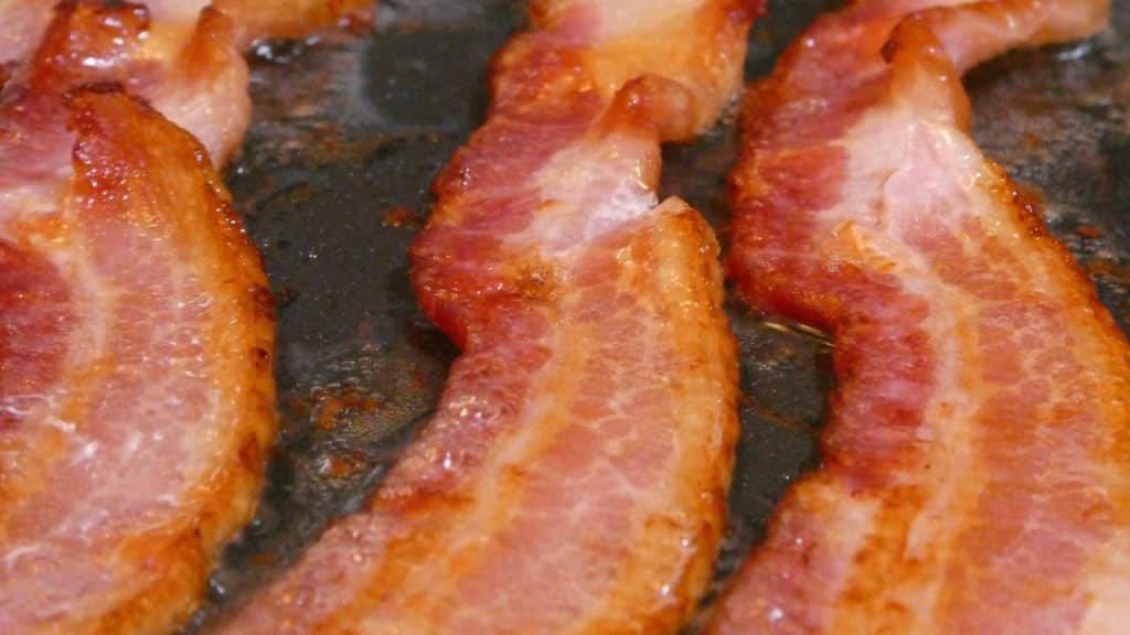 A close-up of bacon strips sizzling in a pan.