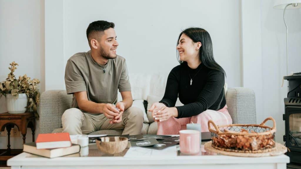 A happy man and woman are talking and smiling on a sofa.