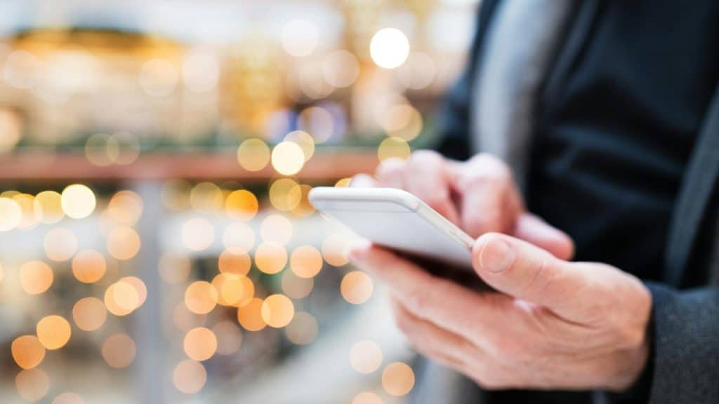 A person’s hands holding a smartphone against a backdrop of blurred lights.