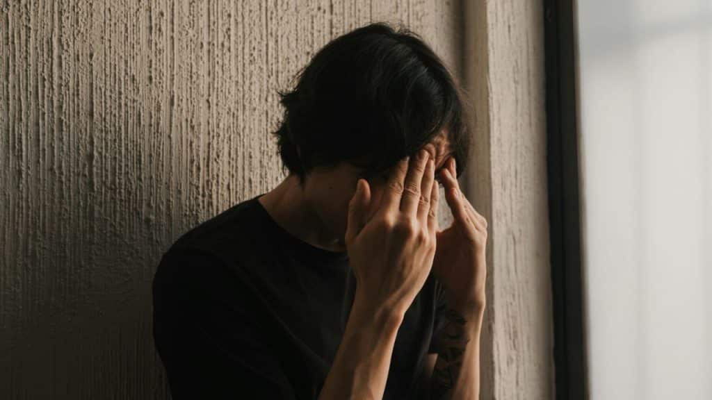 A person with dark hair covers their face with their hands, looking distressed.