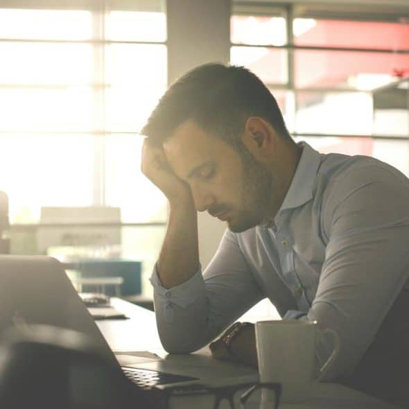 A man slumped over his laptop at a desk.