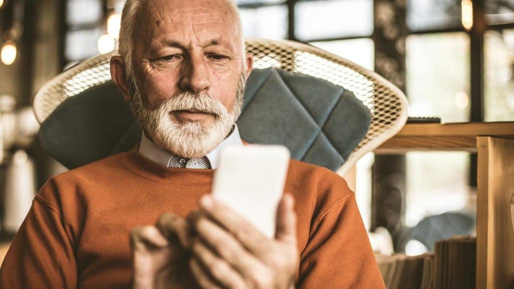 An elderly man intently using a smartphone.