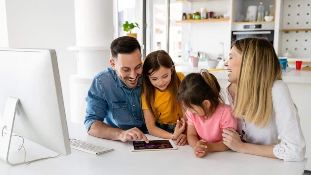 A family of four gathered around a tablet at the kitchen table.