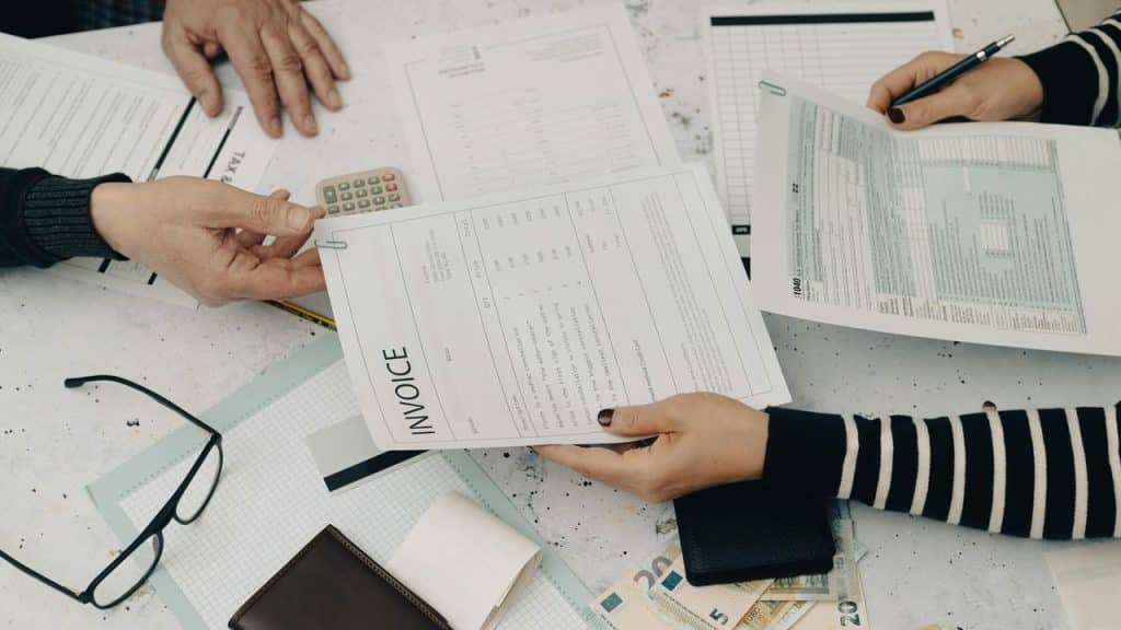 An invoice being exchanged over a desk with documents, cash, and a calculator.