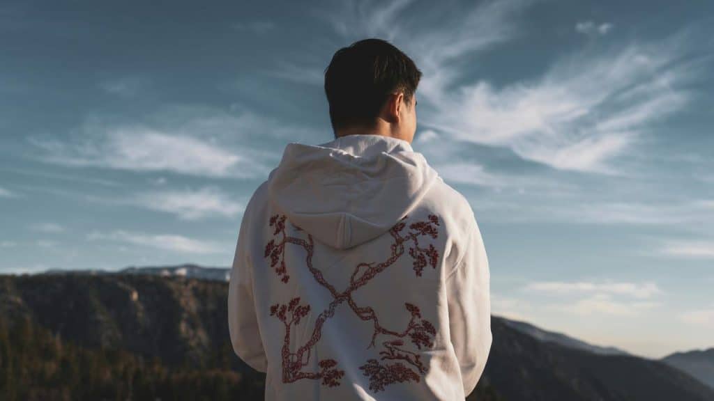 A man in a white hoodie looking out over a mountain landscape.