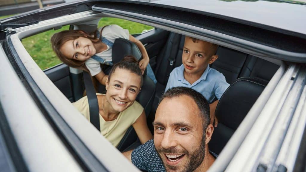 A family of four smiling through a car’s open sunroof.
