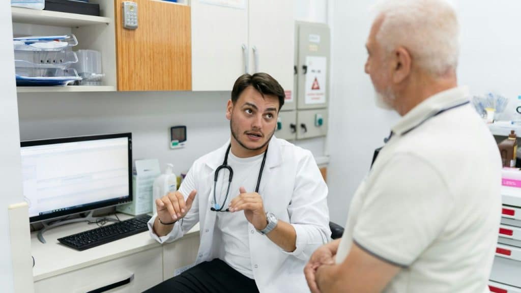 A doctor in a white coat talks to an older man with white hair in an office.