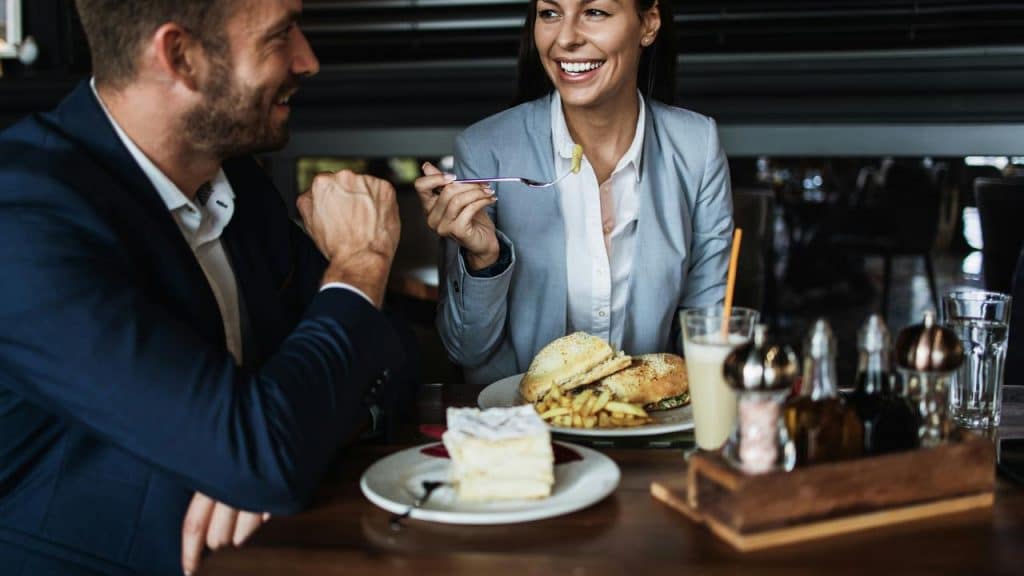 A businesswoman eating fries and chatting with a man in a suit.