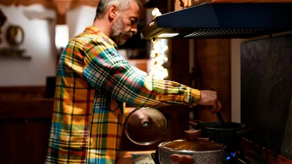 A man stirring a pot on a stovetop in a cozy kitchen.