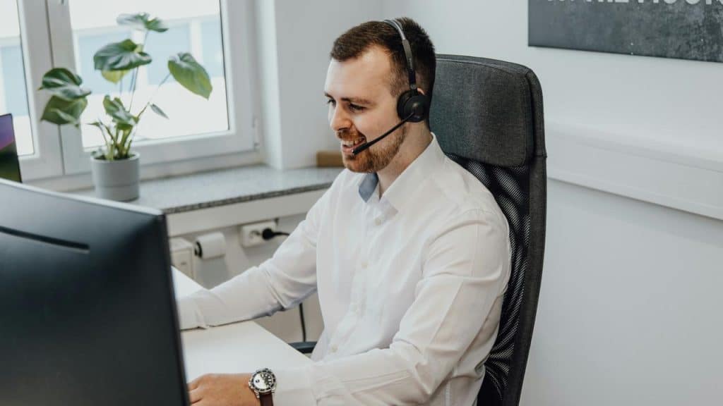 A man wearing a headset and smiling at a computer monitor.