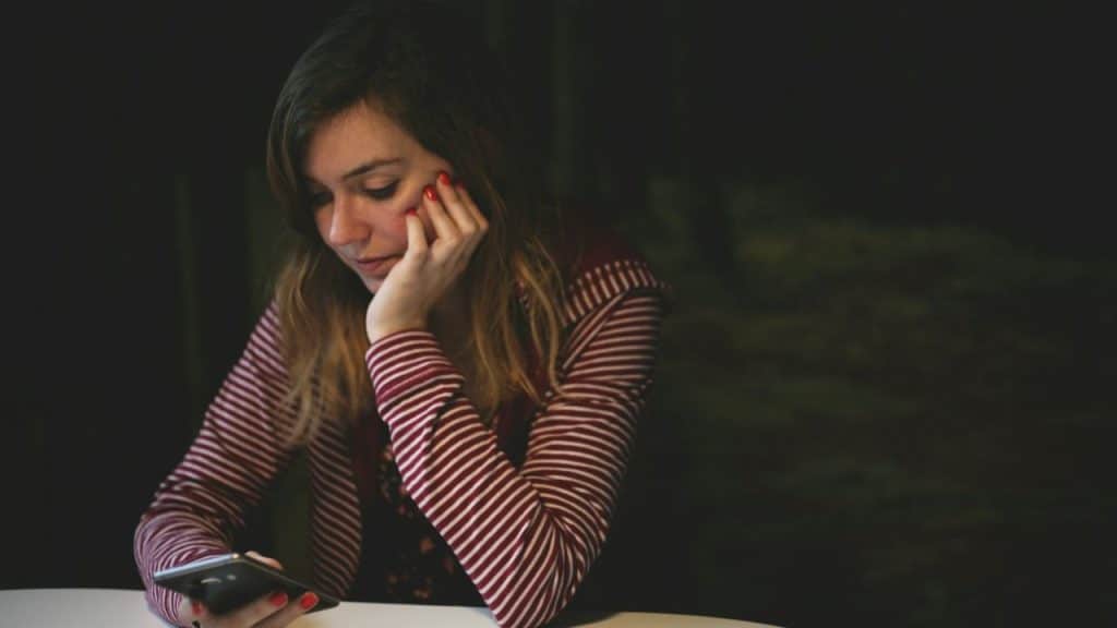 A woman with red nail polish looks at her phone, resting her chin on her hand.