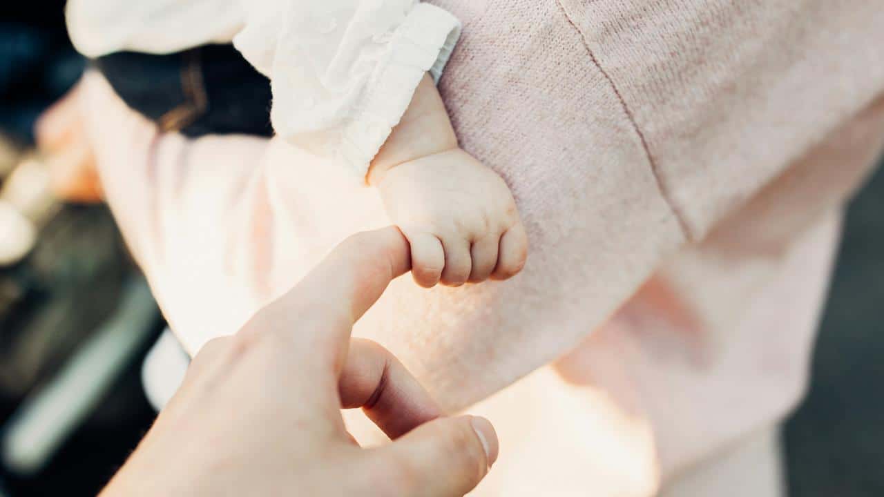 A baby’s hand grasping an adult’s finger.