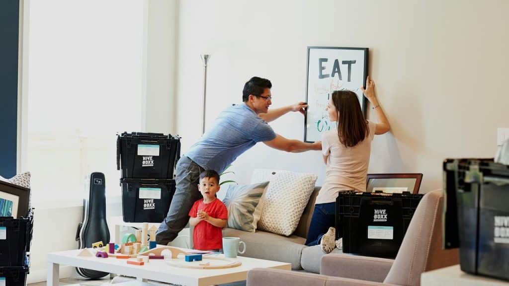 A family hanging a framed sign in a room full of unpacked moving boxes.