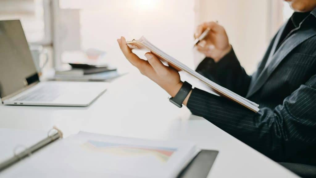 A businessperson writing on a clipboard at a desk.