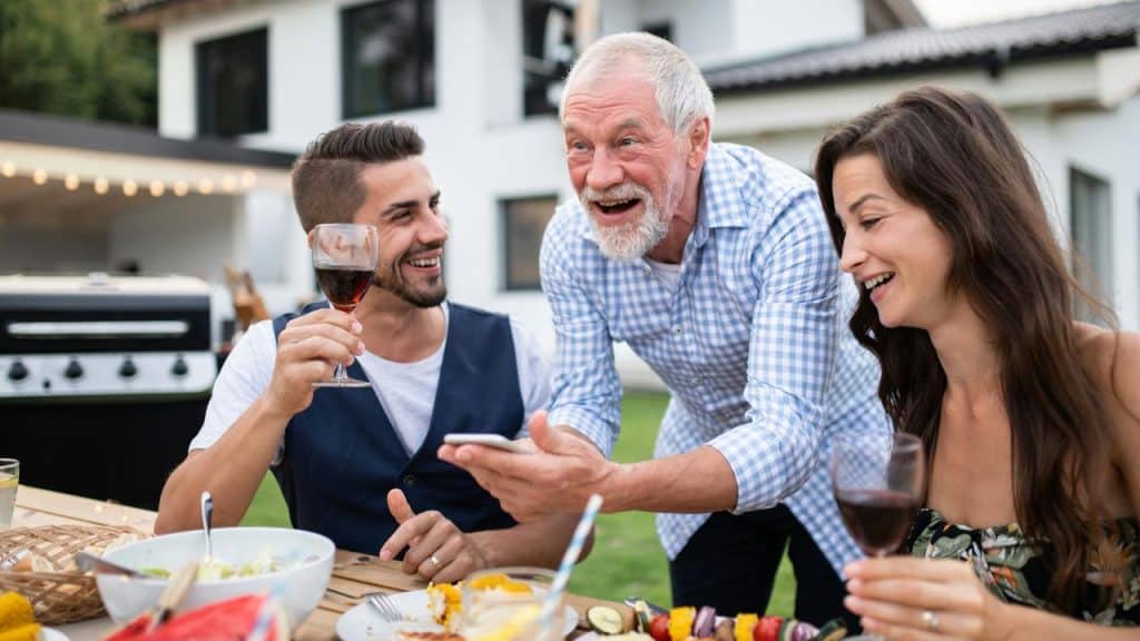 A man showing a phone to two friends enjoying wine outdoors.