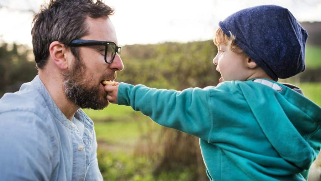A child feeding his father a snack outdoors.