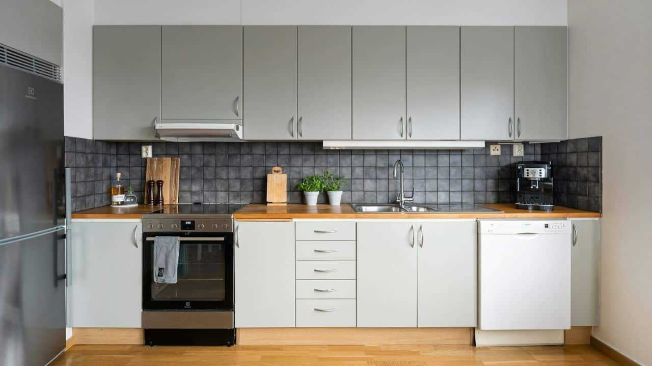 A contemporary kitchen features light grey cabinets, dark tile backsplash, and wooden countertops.
