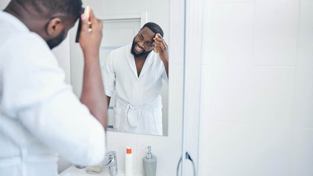 A man in a bathrobe wiping his face in a mirror.