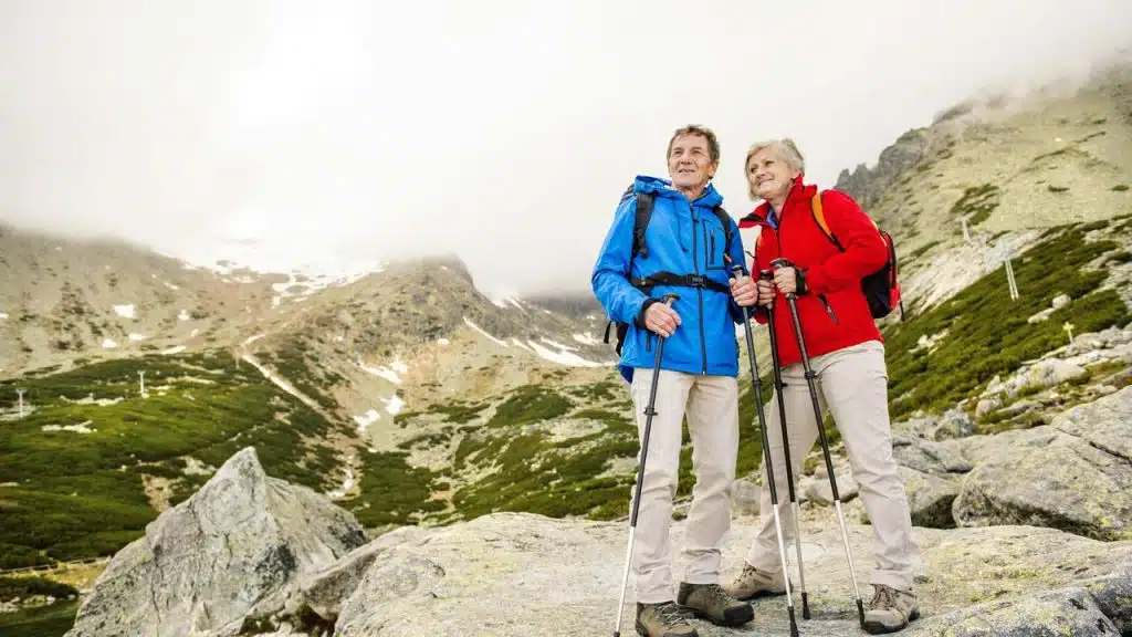 A senior couple with hiking poles on a rocky mountain path.