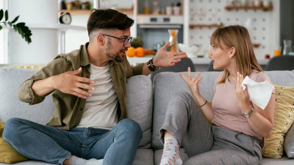A man and woman are intensely arguing on a couch in a living room.
