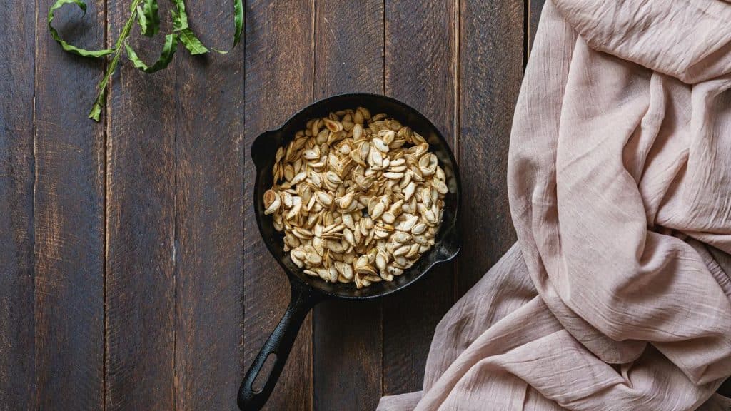 A cast iron skillet filled with roasted pumpkin seeds on a wooden surface.