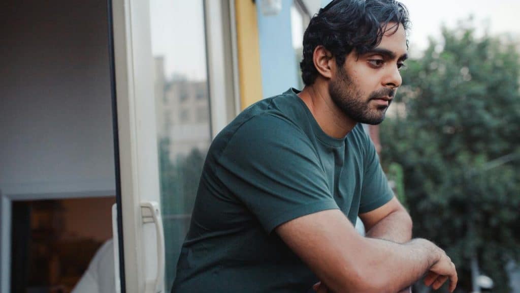 A man leaning on a balcony railing looking thoughtful.