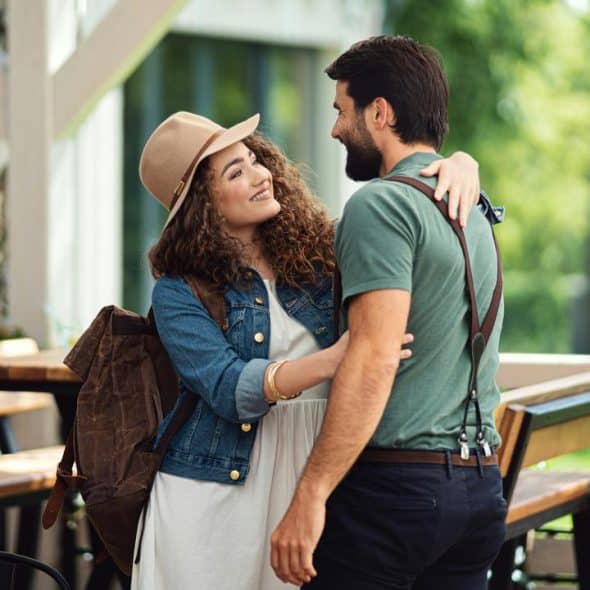 A woman in a hat and denim jacket hugging a bearded man