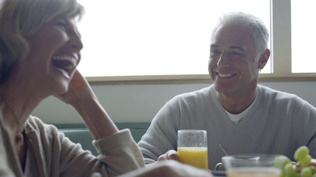 A laughing woman looks at a smiling man holding a glass of orange juice.