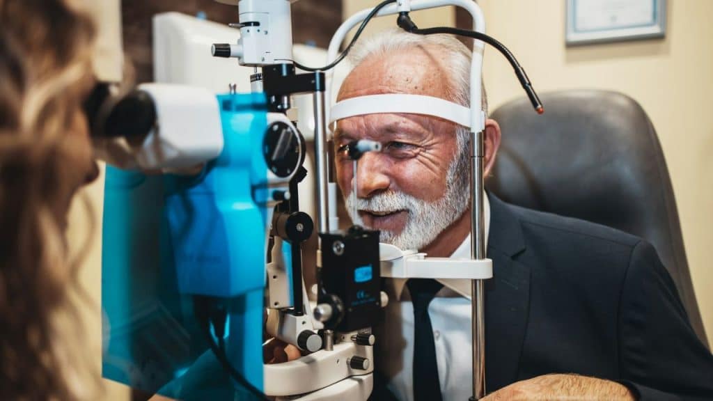 A smiling elderly man undergoes an eye exam on an optical machine.