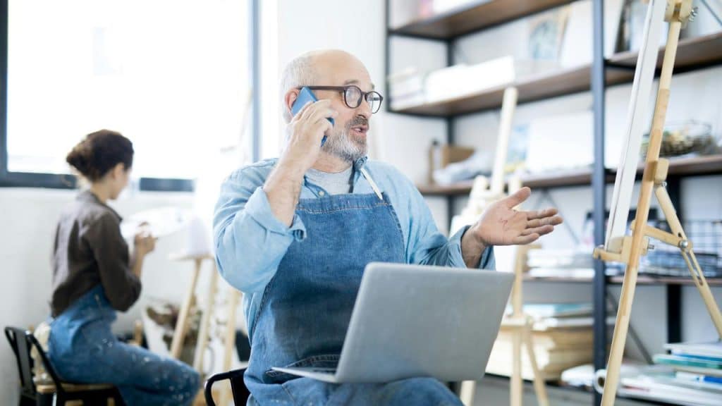 An older artist talking on a phone in his studio.