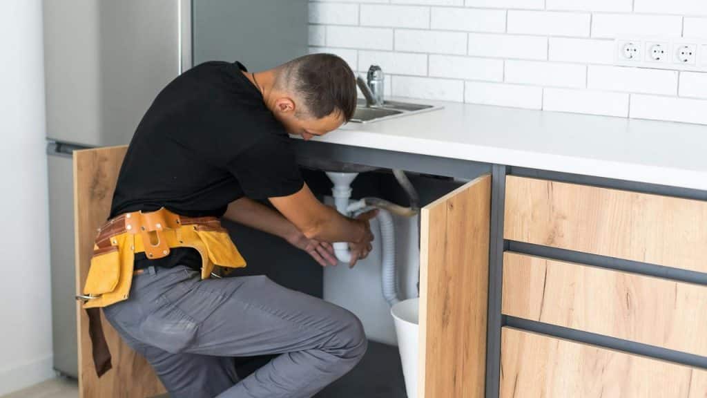 A plumber working on a kitchen sink drain.