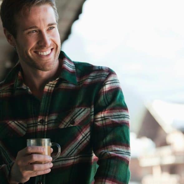 A smiling man in a plaid shirt holding a mug.