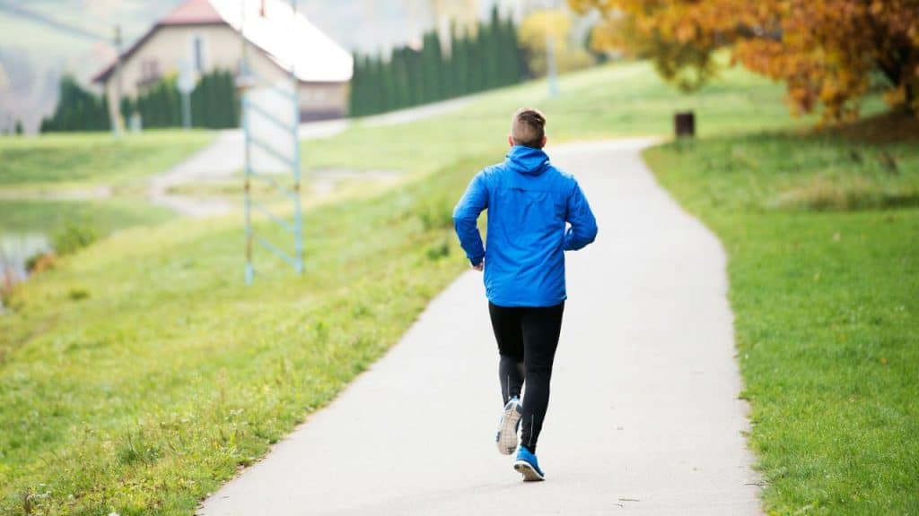 A person in a blue jacket and black pants runs down a paved path.