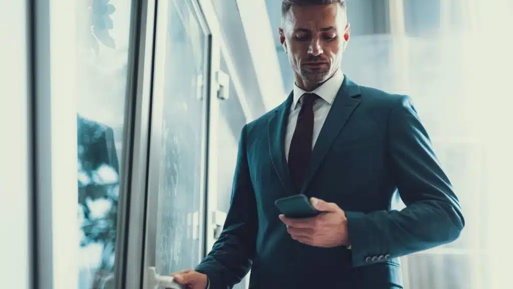 A businessman checking his phone while opening a glass door.