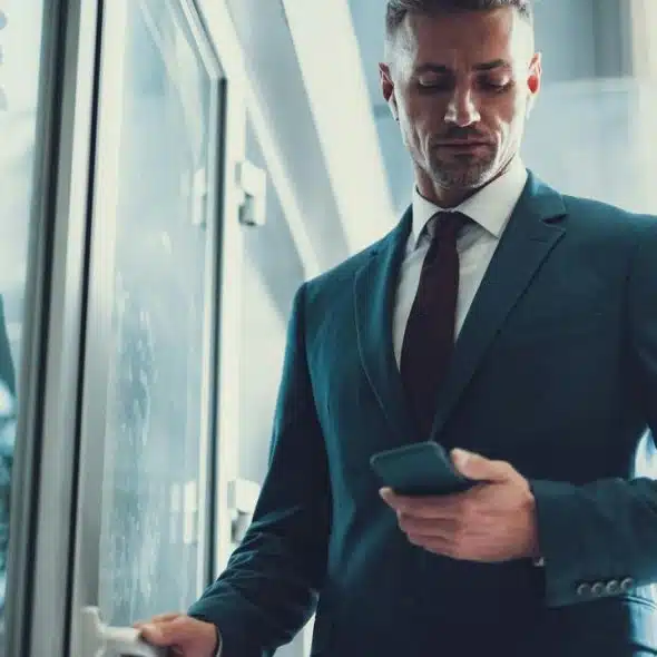 A businessman checking his phone while opening a glass door.