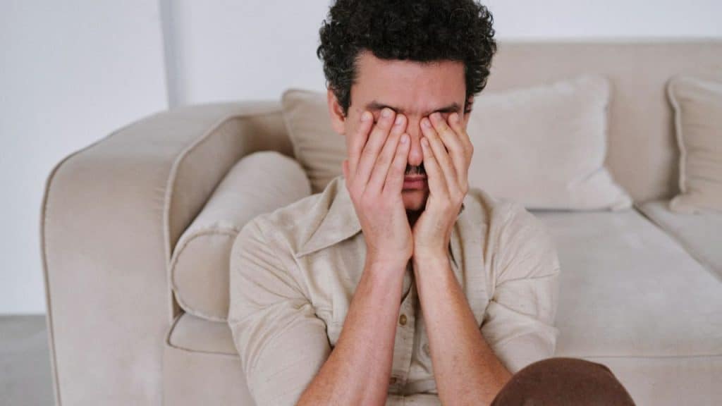 A man with curly hair covers his face with both hands, looking distressed.