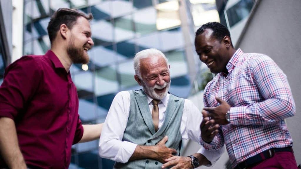 A candid shot of three diverse men laughing heartily outdoors in front of a modern building.