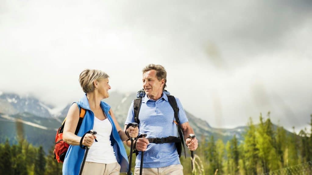 A senior couple hiking in the mountains with trekking poles.