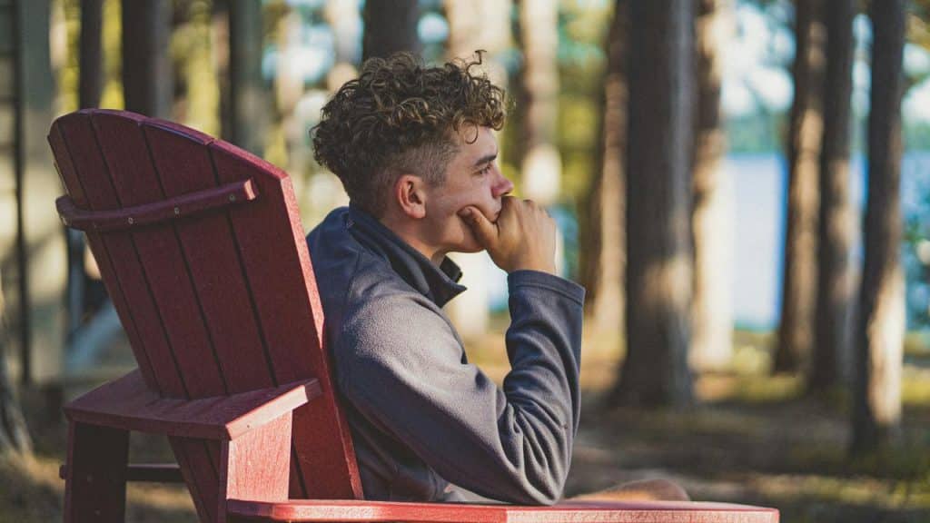 A man seated in a red outdoor chair, gazing thoughtfully.