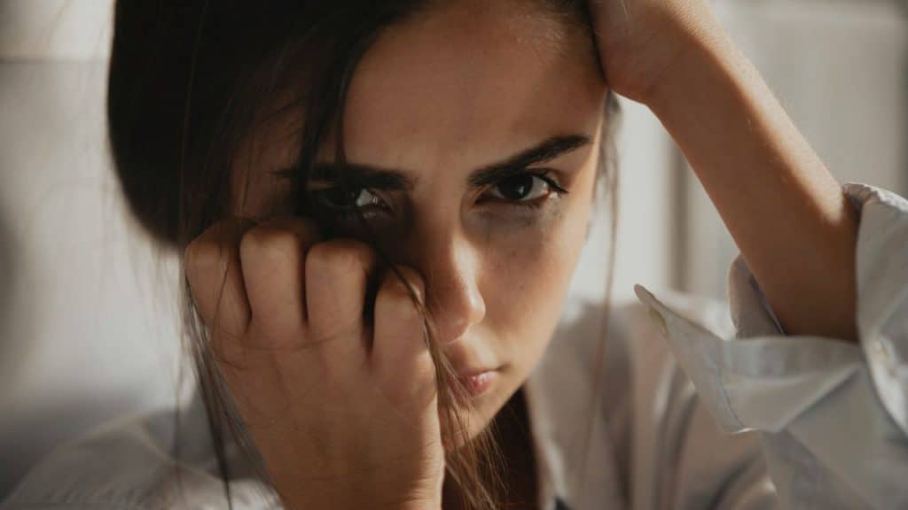 A woman with smudged eye makeup looks intensely at the camera, holding her hair.