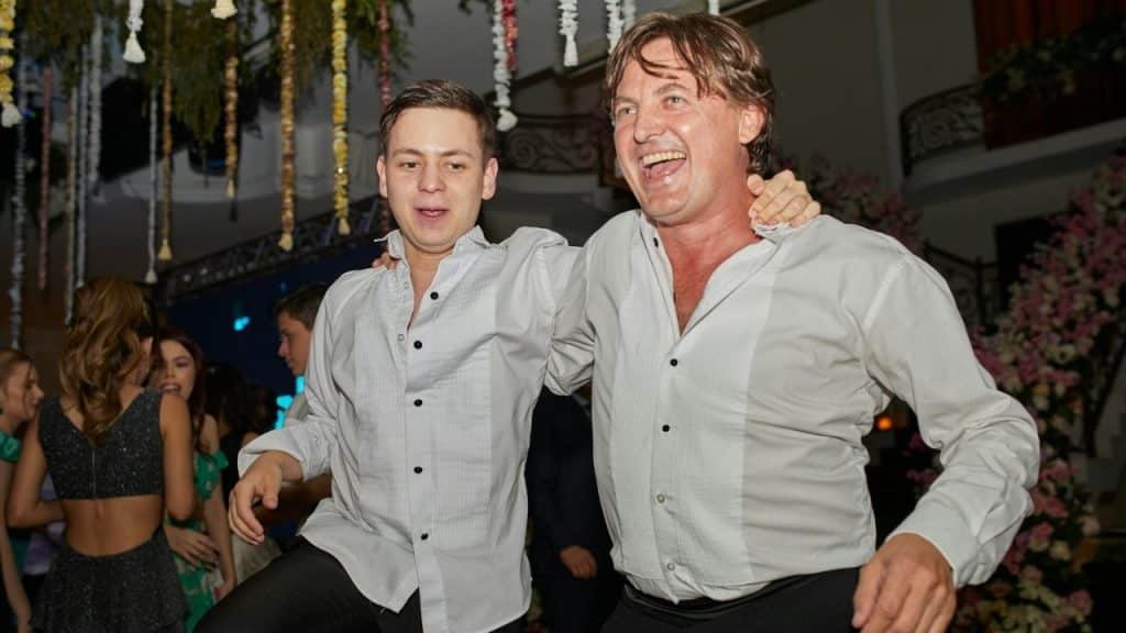 Two men in white shirts and black pants smile and pose at a party.