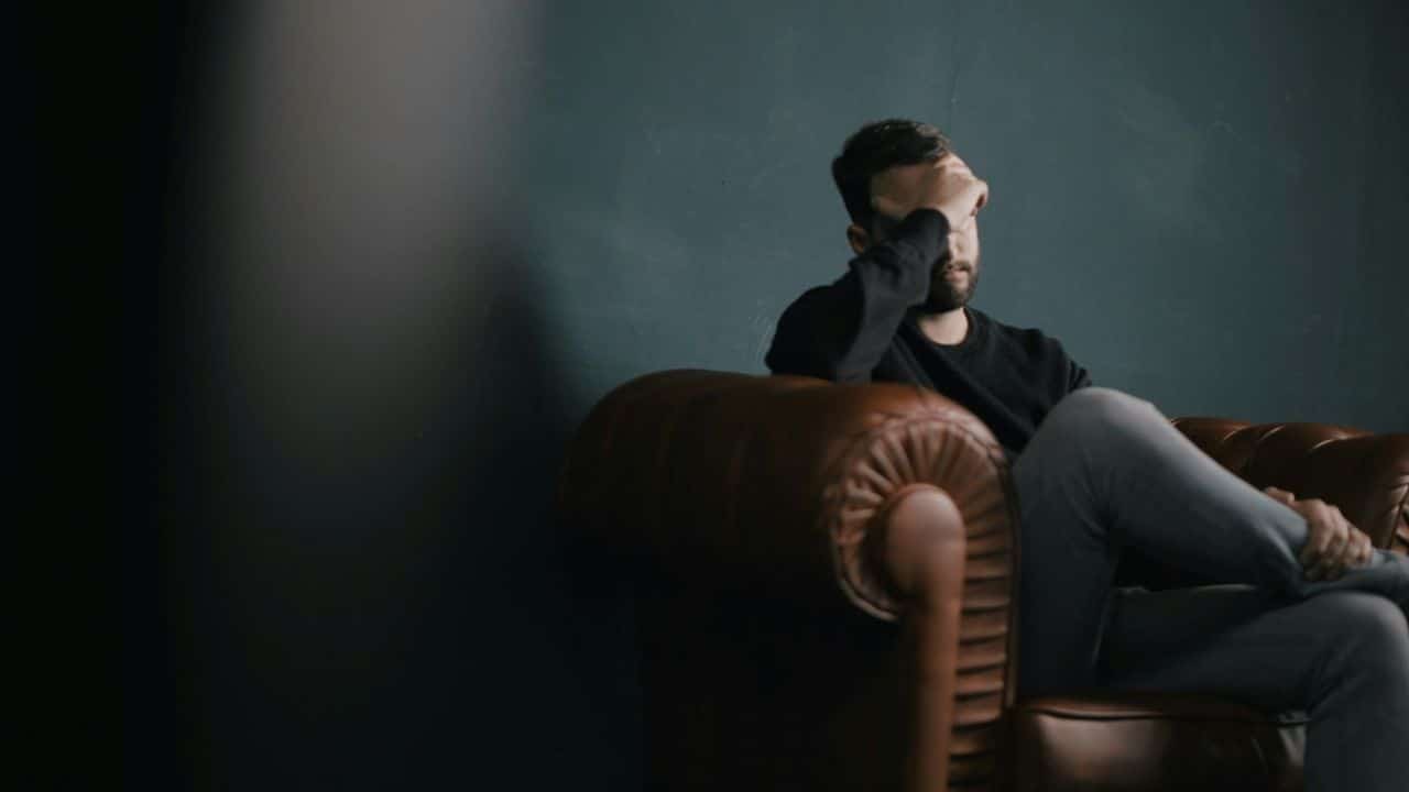 A man sits in a leather armchair with his hand covering his face.