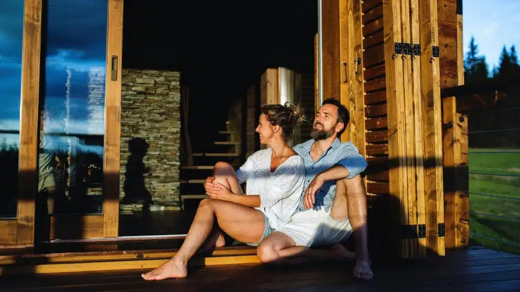 A couple relaxing on a wooden porch in warm sunlight.