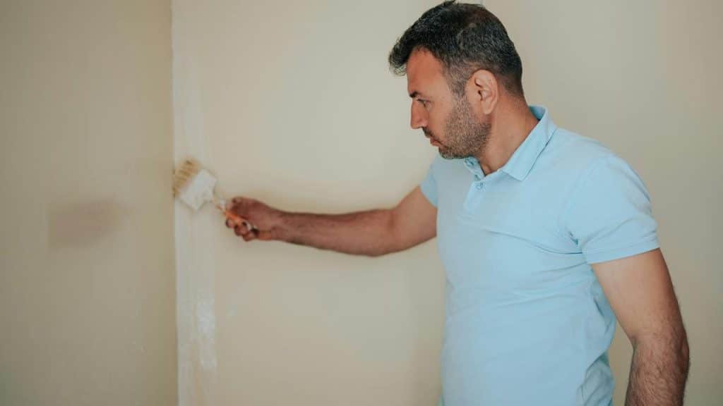 A man painting a wall corner with a brush.