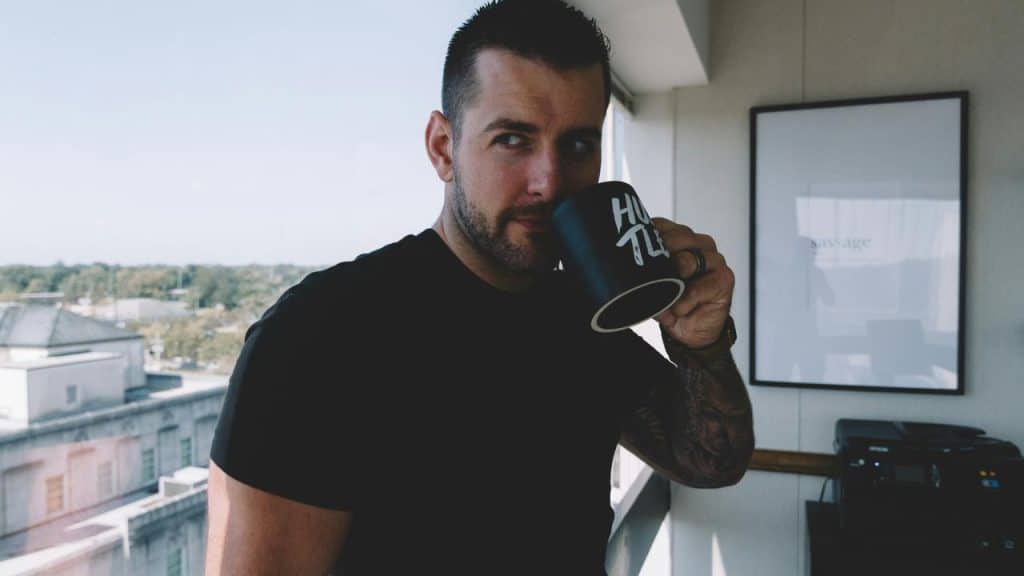 A man sipping coffee from a mug by a window.